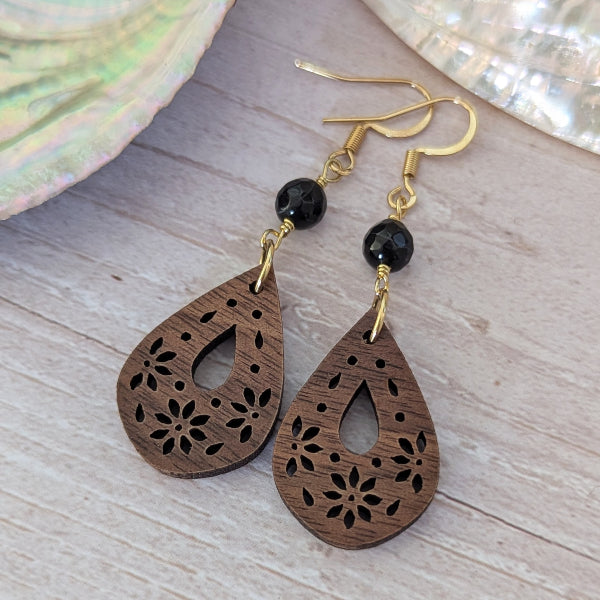 Wooden teardrop earrings with black beads and gold hooks on a wooden surface.