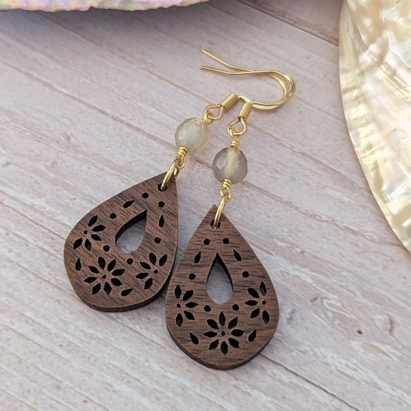 Wooden teardrop earrings with gold hooks and beads on a light wooden surface.