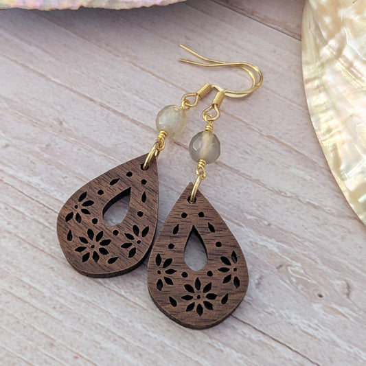 Wooden teardrop earrings with gold hooks and beads on a light wooden surface.