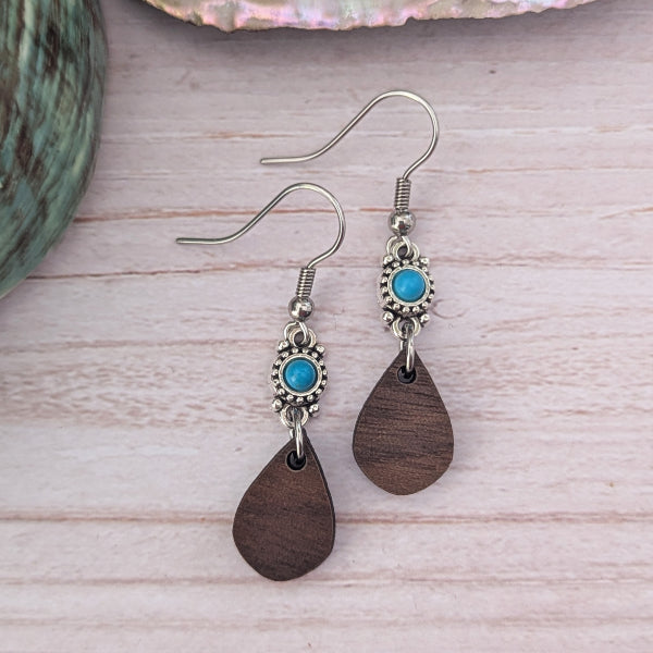 Wooden teardrop earrings with turquoise stones on a light wooden surface