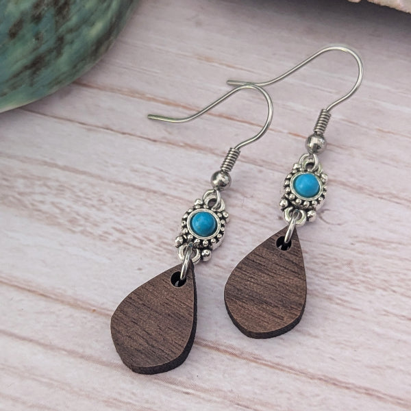 Wooden teardrop earrings with turquoise stones and silver hooks on a light wooden surface.