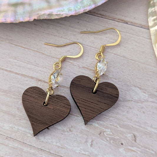 Wooden heart-shaped earrings with gold hooks and clear crystals on a light wooden surface.