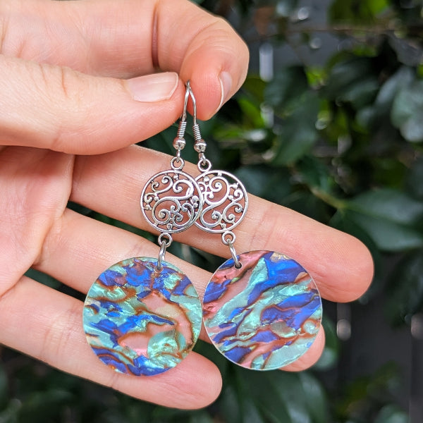 Hand holding a pair of earrings with colorful circular designs and silver filigree.
