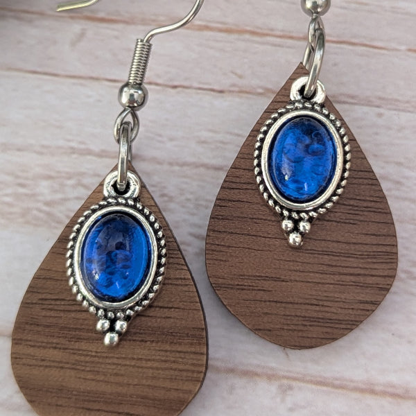 Wooden teardrop earrings with blue stones and silver accents on a light wooden surface.