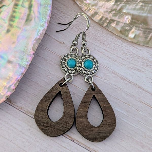 Wooden teardrop earrings with turquoise stones and silver hooks on a wooden surface. Stainless steel hooks.