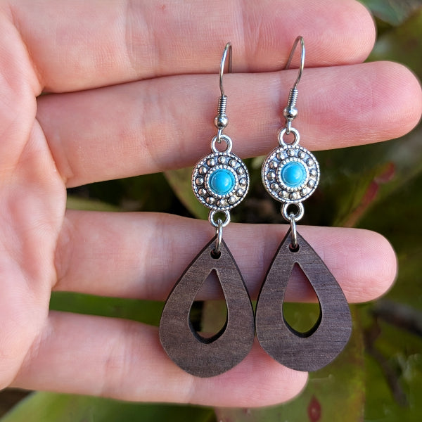 Wooden teardrop earrings with turquoise stones and silver hooks on a hand. Stainless steel hooks.