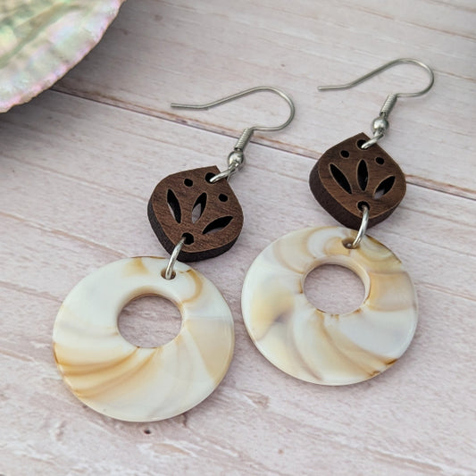 Pair of earrings with wooden and shell-like designs on a wooden surface