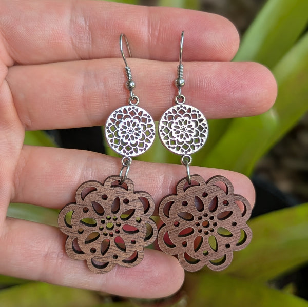 Wooden floral earrings held between fingers with a natural background. Stainless steel hooks.
