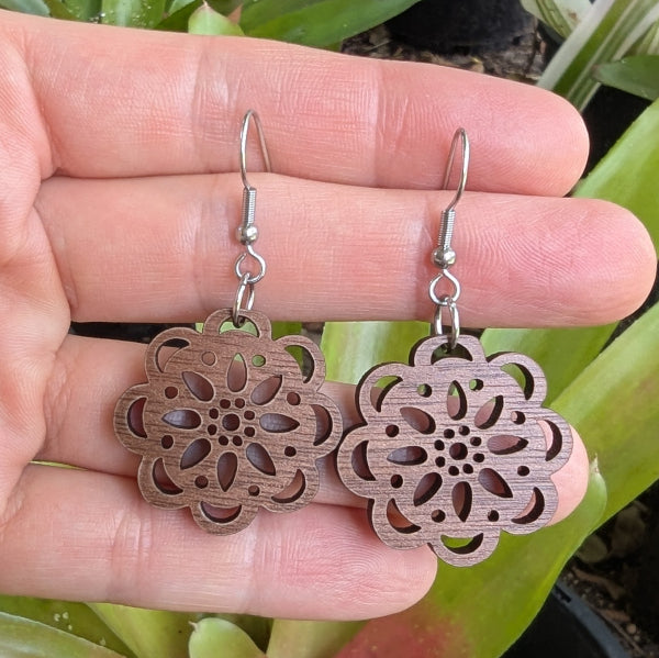 Wooden floral earrings held in a hand with a natural background. Stainless steel hooks.