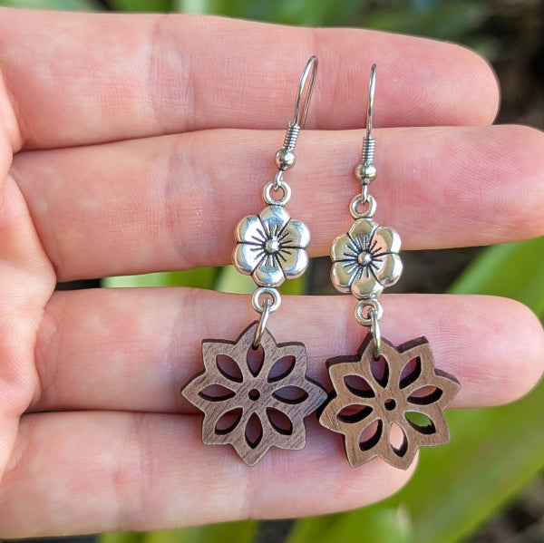 Wooden floral earrings with silver accents held on a hand. Stainless steel hooks.