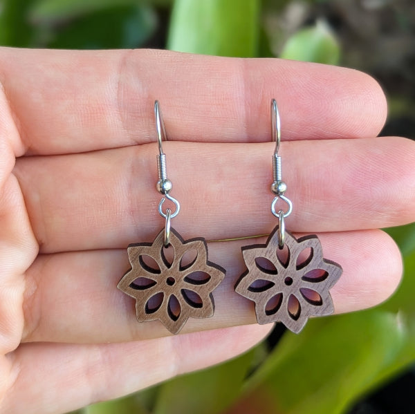 Floral-patterned earrings held in a hand with a natural background. Stainless steel hooks.