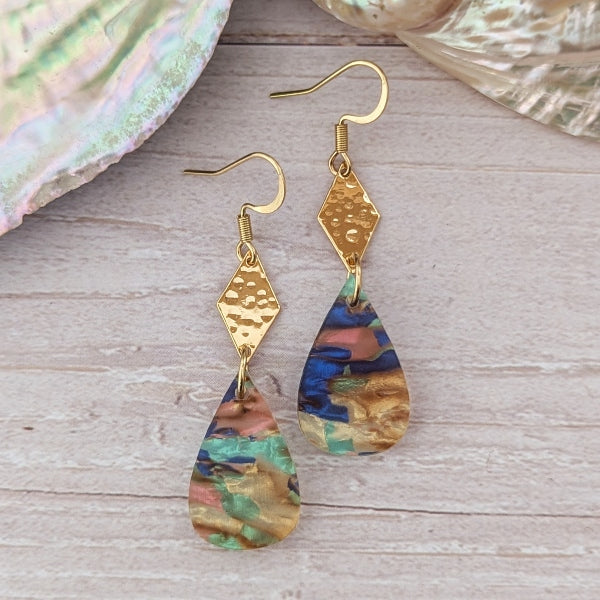 Gold earrings with teardrop-shaped, multicolored shapes on a wooden surface.