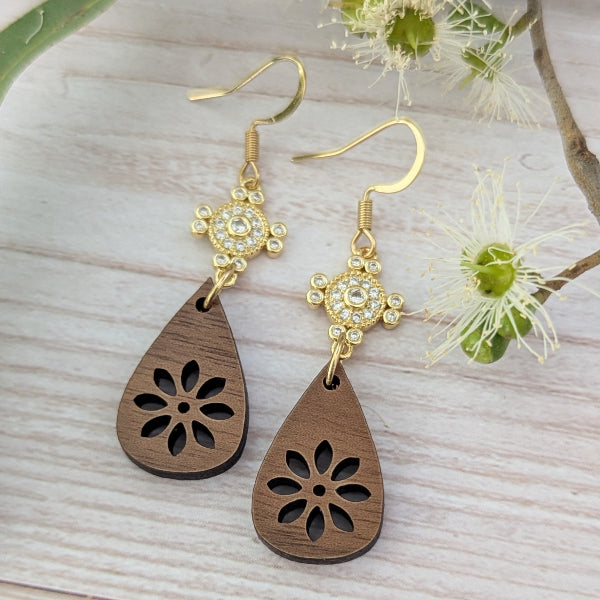 Wooden teardrop earrings with crystal and gold accents on a light wooden surface with flowers. Gold plated stainless steel hooks.