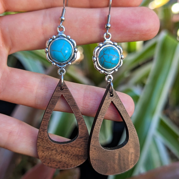 Wooden teardrop earrings with turquoise stones held between fingers against a blurred natural background. Stainless steel hooks.