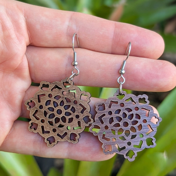 Wooden floral earrings held in a hand with a natural background. Stainless steel hooks.