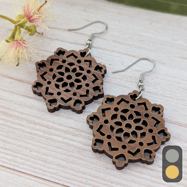 Wooden floral earrings on a light wooden surface with a blurred flower in the background. Stainless steel hooks.