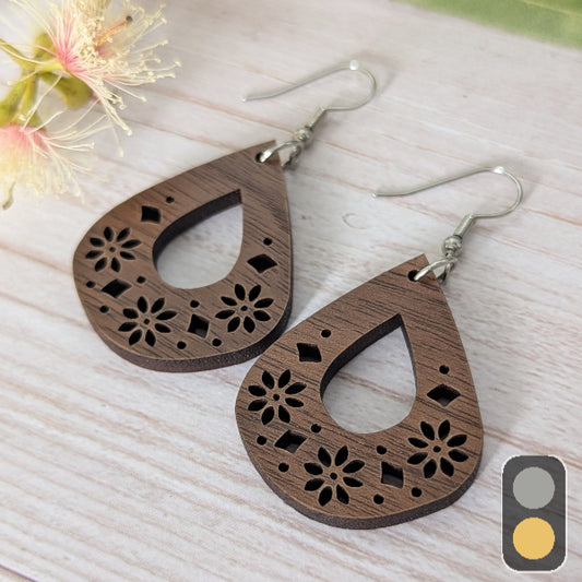 Wooden teardrop-shaped earrings with floral cutouts on a light wooden surface. Stainless steel hooks.