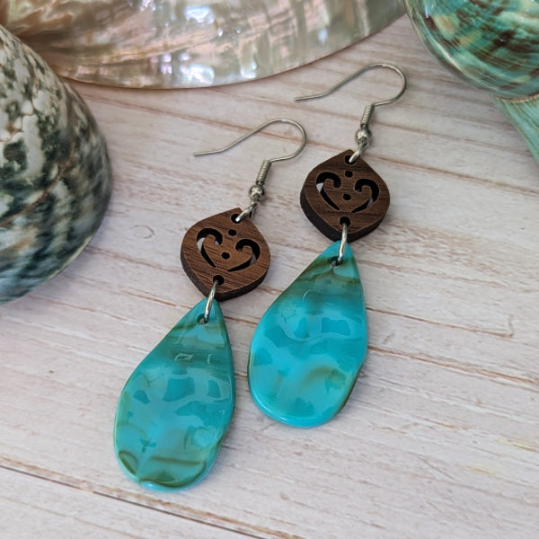 Resin turquoise coloured teardrop earrings with wooden accents on a light wood surface. Stainless steel hooks.