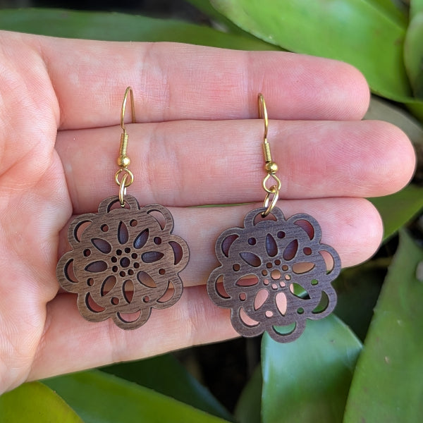 Wooden floral earrings held in a hand with a natural background. Gold plated stainless steel hooks.