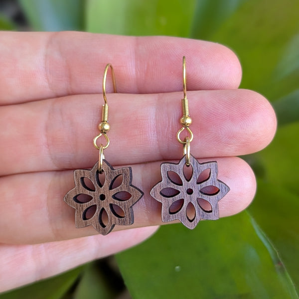 Pair of floral-patterned earrings held between fingers with a natural background. Gold plated stainless steel hooks.
