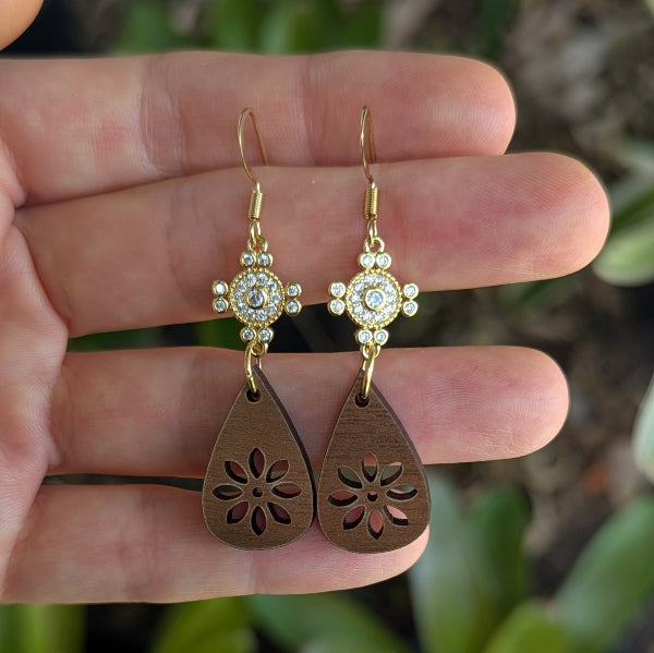 Wooden teardrop earrings with crystal and gold accents held on a hand. Gold plated stainless steel hooks.