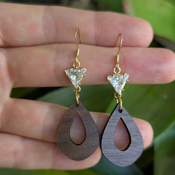 Wooden teardrop earrings with gold and crystal accents held in a hand. Plated gold stainless steel hooks.