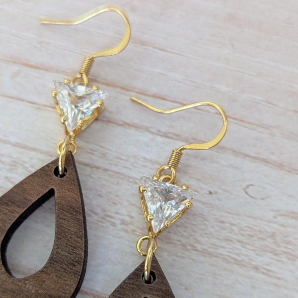Wooden teardrop earrings with gold and crystal accents on a light wooden surface. Plated gold stainless steel hooks.
