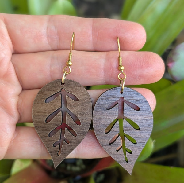 Wooden leaf-shaped earrings held in a hand with a natural background. Gold plated stainless steel hooks.