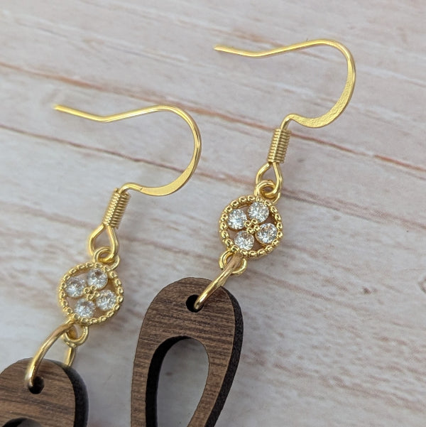 Wooden drop earrings with gold and crystal accents on a light wooden surface. Plated gold stainless steel hooks.