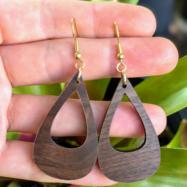 Wooden teardrop earrings held between fingers with a natural background. Gold plated stainless steel hooks.