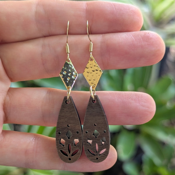Gold and wooden earrings held between fingers with a blurred green background. Plated gold stainless steel hooks.