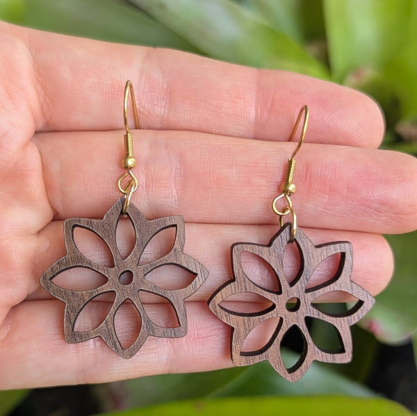 Wooden flower-shaped earrings on a hand with a natural background. Gold plated stainless steel hooks.