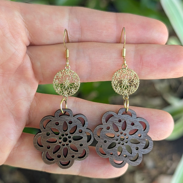 Gold and wooden floral earrings held in a hand with a natural background. Gold plated stainless steel hooks.