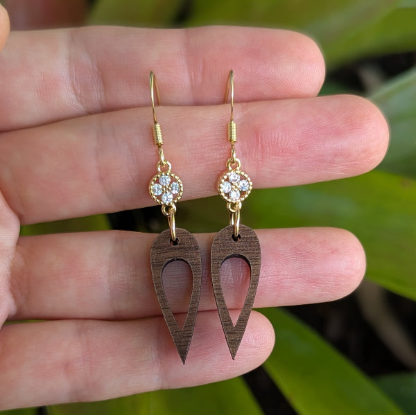 Wooden drop earrings with gold and crystal accents held on a hand. Plated gold stainless steel hooks.