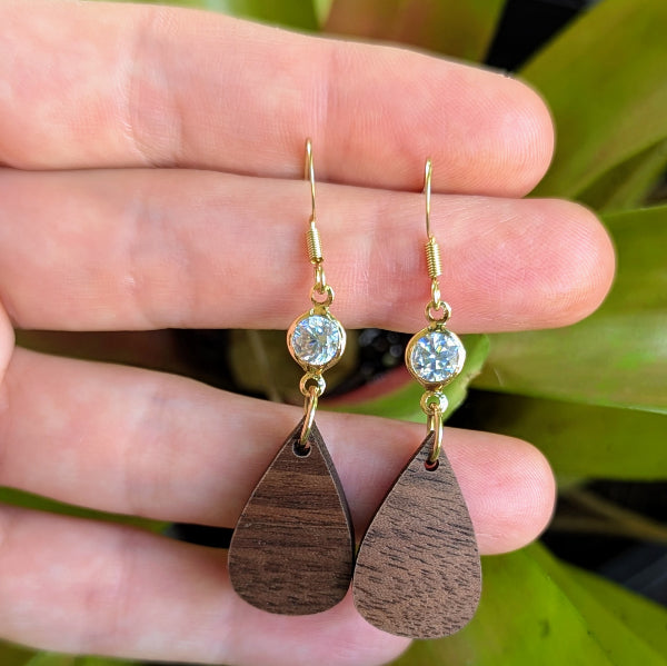 Wooden teardrop earrings with gold and crystal accents held in a hand. Gold plated stainless steel hooks.