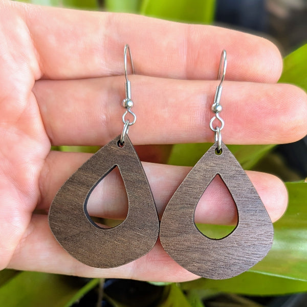 Wooden teardrop earrings held in a hand with a natural background. Stainless steel hooks.