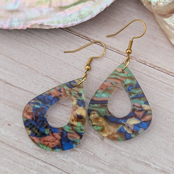 Multicolored earrings on a wooden surface with seashells in the background