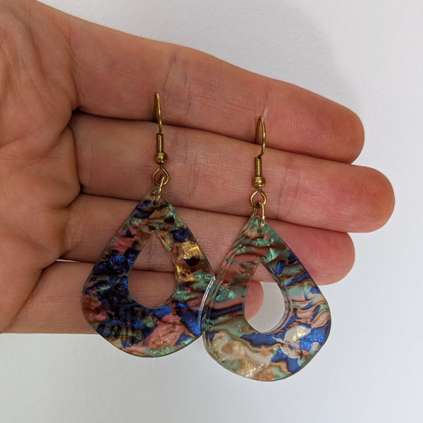 Colorful teardrop-shaped earrings held in a hand against a white background