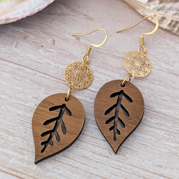 Wooden leaf-shaped earrings with gold hooks on a wooden surface