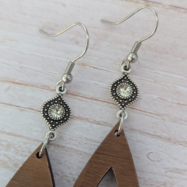 Wooden teardrop earrings with silver toned connectors with crystals, stainless steel hooks on a light wooden surface.