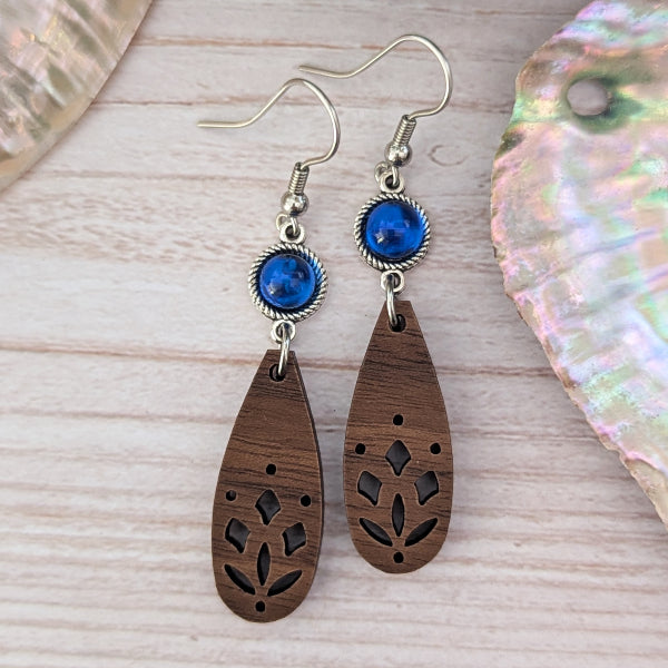 Wooden teardrop earrings with blue stones on a wooden surface