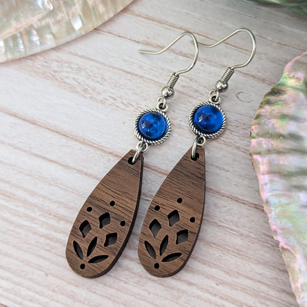 Wooden teardrop earrings with blue stones on a light wooden surface