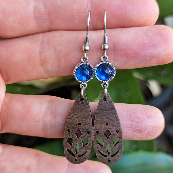 Wooden earrings with blue stones held between fingers against a natural background