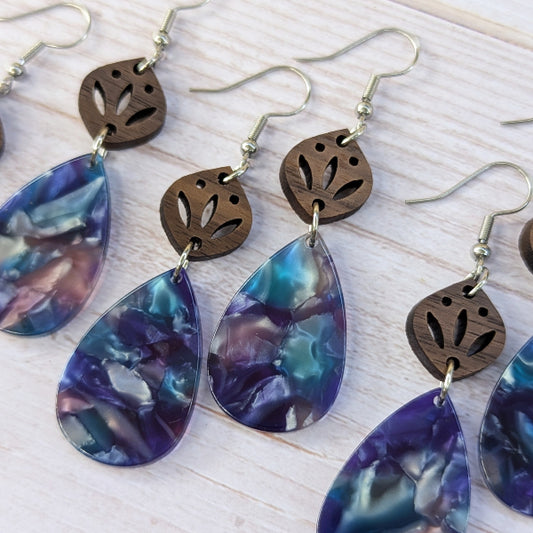 Earrings with purple teardrop-shaped stones and brown leaf-like connectors on a light wooden surface.