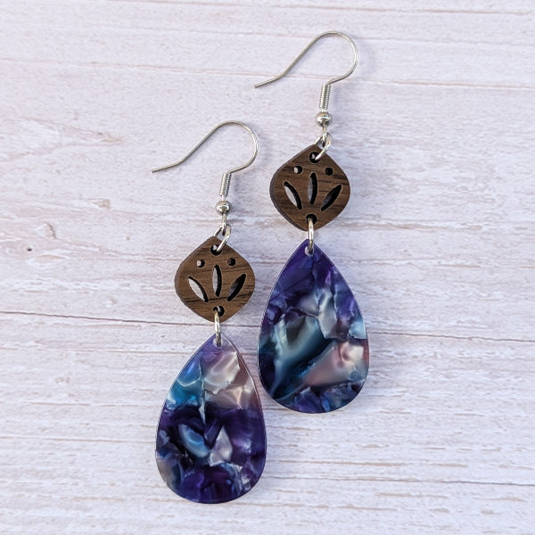 Pair of earrings with purple teardrop-shaped stones and brown leaf-like tops on a light wooden surface.