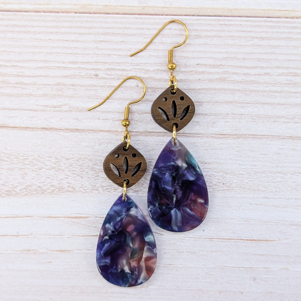Purple teardrop earrings with gold accents on a light wooden surface