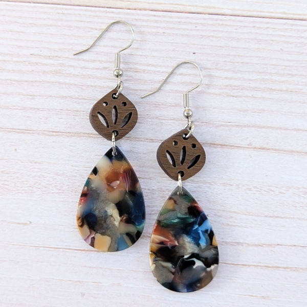 Pair of earrings with teardrop-shaped multicolored drops and wooden accents on a light wood background.