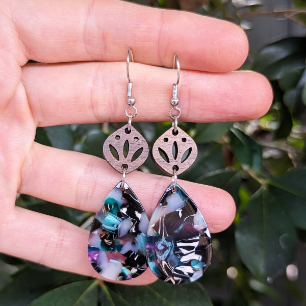 Teardrop-shaped earrings with floral design on a hand against a green leafy background