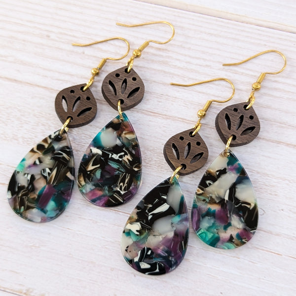 Two pairs of earrings with floral teardrop design and leaf-shaped wooden elements on a light wood background.