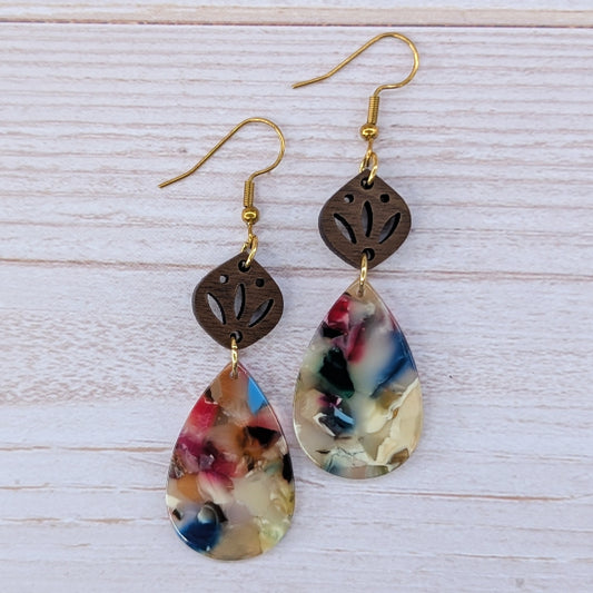 Pair of earrings with teardrop-shaped colorful drops and gold hooks on a light wooden surface.
